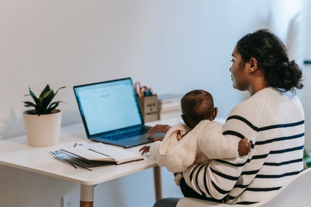 thoughtful ethnic woman sitting with baby and working on laptop