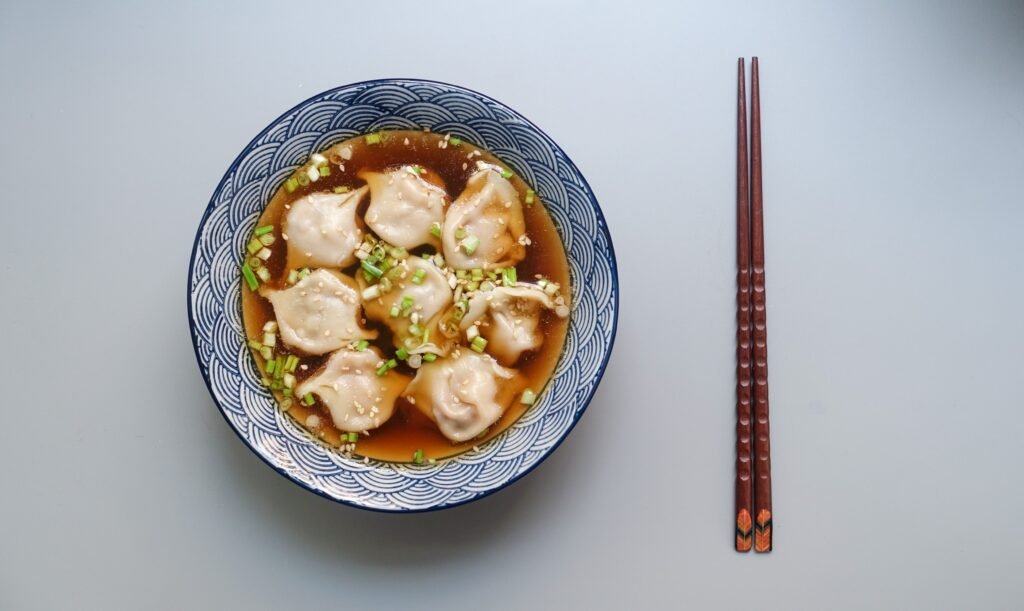dumplings in a bowl of broth with chopsticks