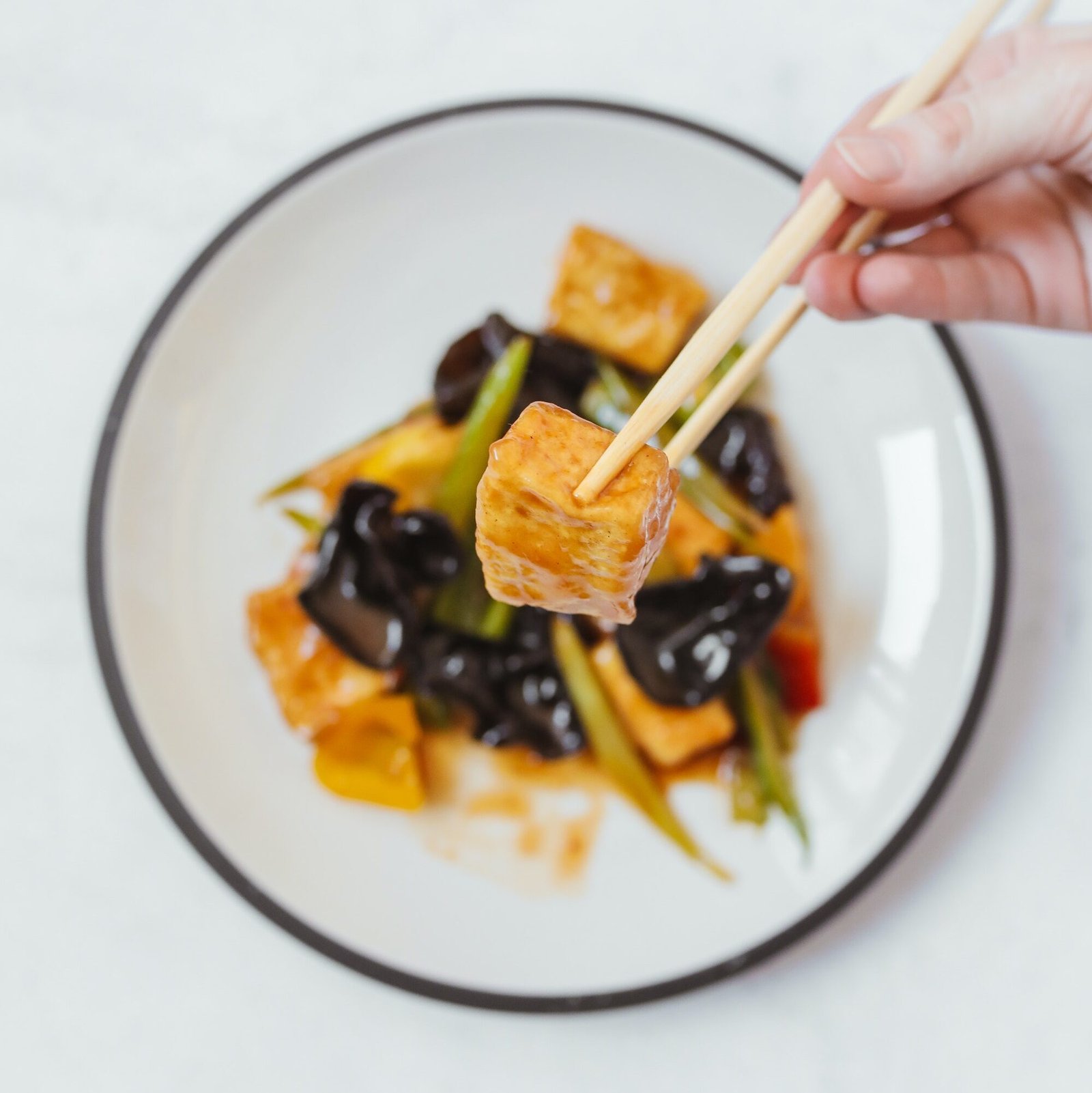 piece of sweet and sour tofu held in chopsticks chinese food